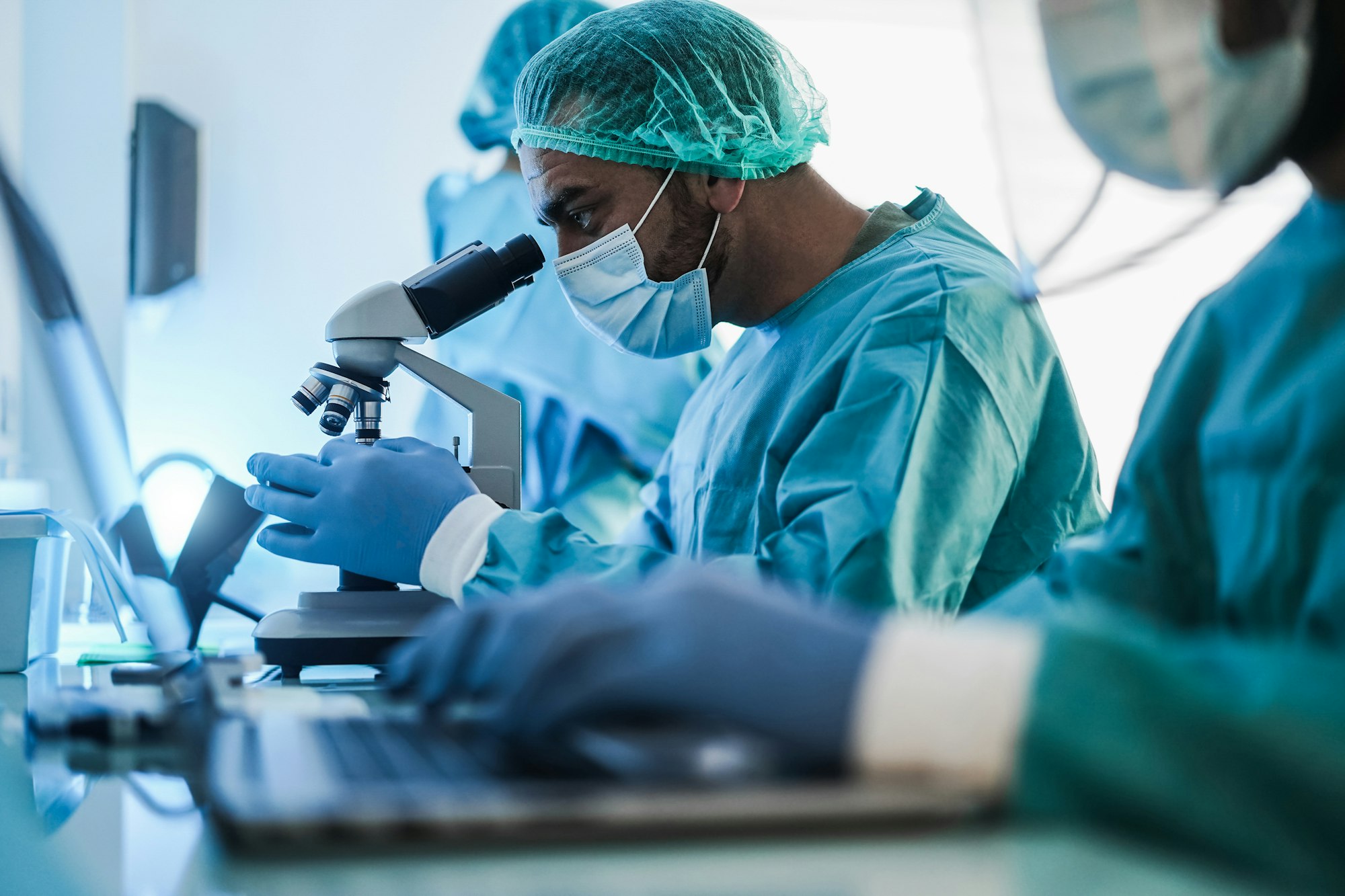 Medical scientist in hazmat suit working with microscope and laptop computer inside laboratory