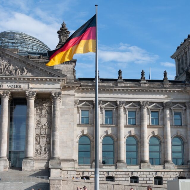 people walking beside building with waving flag of Germany on pole