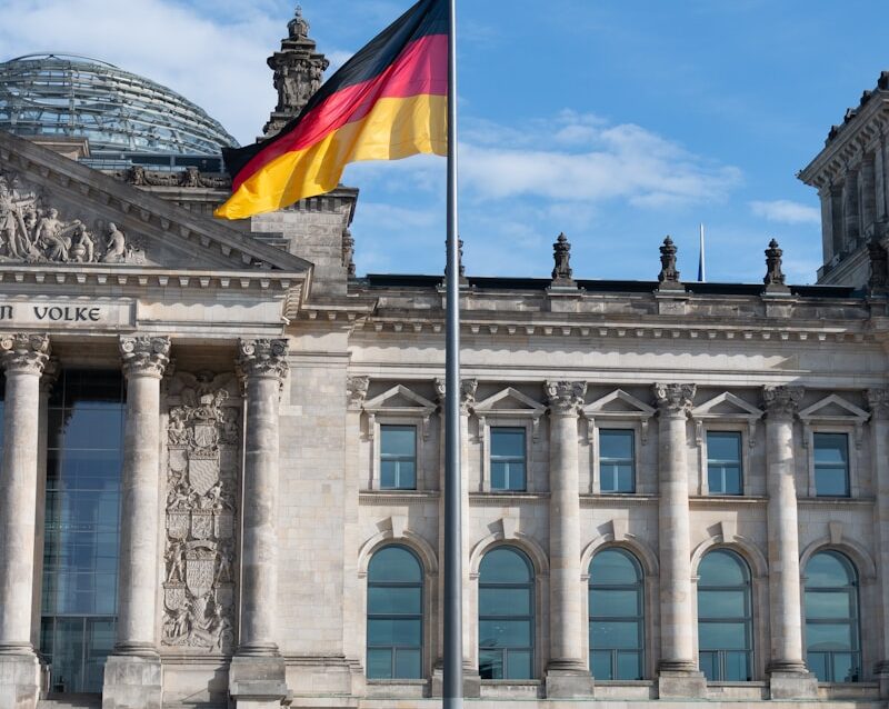 people walking beside building with waving flag of Germany on pole